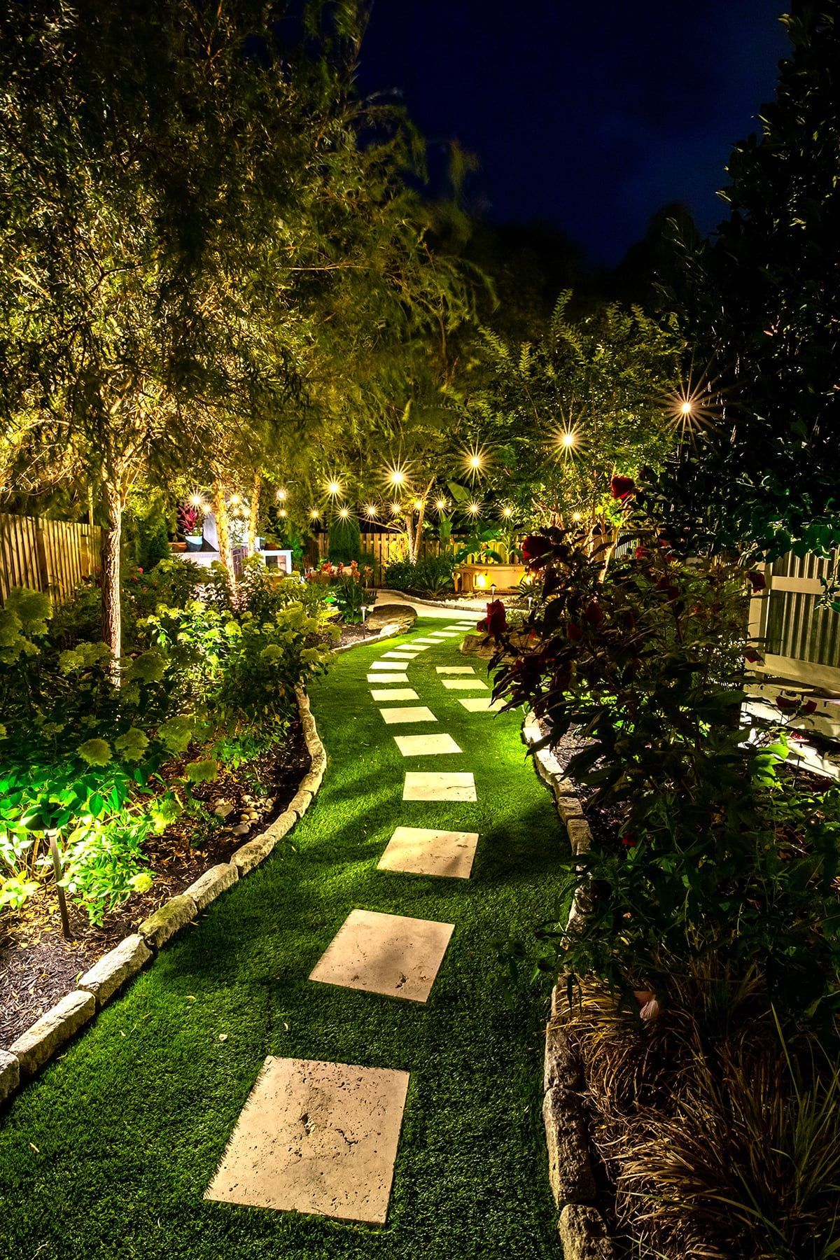 Stepping-stone garden path lit by string lights and path lights at night